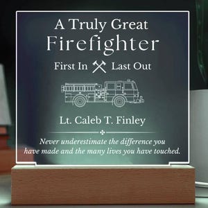 Puede incluir: Una placa de acrílico blanco con una base de madera negra. La placa tiene un contorno blanco de un camión de bomberos y el texto "A Truly Great Firefighter First In Last Out Lt. Caleb T. Finley Never underestimate the difference you have made and the many lives you have touched."
