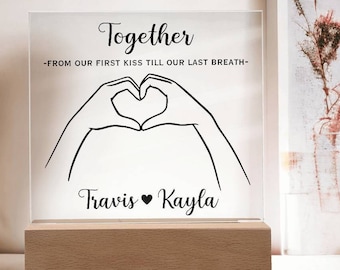 May include: A clear acrylic sign with the text "Together -From our first kiss till our last breath- Travis ♥ Kayla" and a black line drawing of two hands forming a heart shape.