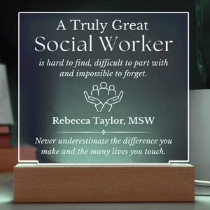 May include: A white acrylic plaque with a blue background and the text "A Truly Great Social Worker is hard to find, difficult to part with and impossible to forget."  The plaque also includes a symbol of two hands holding three people and the text "Rebecca Taylor, MSW" and "Never underestimate the difference you make and the many lives you touch."