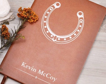 May include: A brown leather journal with a white horseshoe design and the name "Kevin McCoy" embossed on the front.