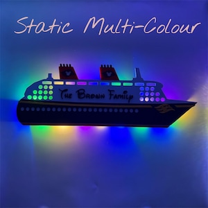Puede incluir: Una l&aacute;mpara LED con forma de barco multicolor. El barco es blanco con detalles en negro y el texto "The Brown Family". Tiene chimeneas rojas y negras con orejas de Mickey Mouse. Las palabras "Static Multi-Colour" est&aacute;n escritas encima del barco.