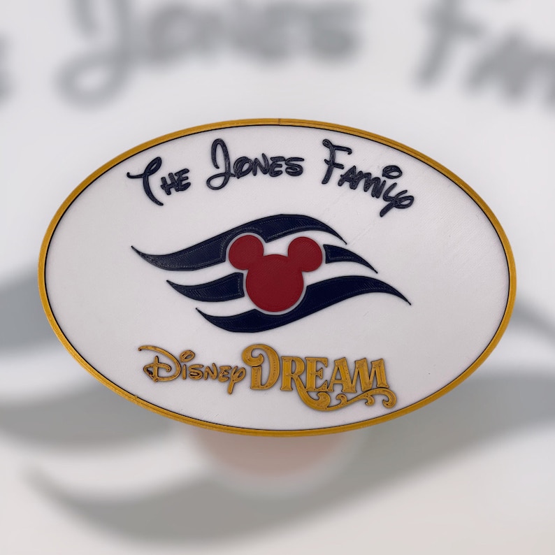 K&ouml;nnte beinhalten: Wei&szlig;er ovaler Pin mit goldener Umrandung. Der Pin zeigt das Disney Dream Logo mit dem Kopf von Mickey Mouse in der Mitte. Der Text "The Jones Family" ist in schwarzer Kursivschrift &uuml;ber dem Logo geschrieben.