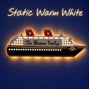 Puede incluir: Una l&aacute;mpara de pared con forma de crucero en negro, blanco y dorado, con el texto "The Brown Family". El barco tiene dos chimeneas rojas con siluetas de Mickey Mouse. Las palabras "Static Warm White" est&aacute;n encima del barco.