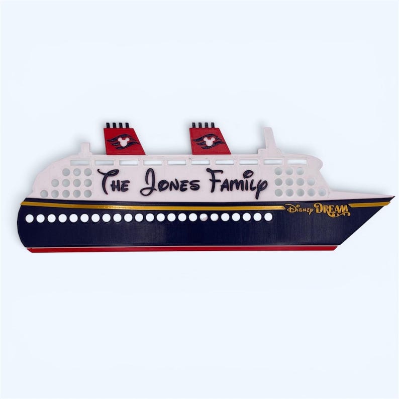 Puede incluir: Un letrero de madera con forma de barco con el texto "The Jones Family" y "Disney DREAM". El letrero presenta un casco blanco con detalles en rojo y negro, y dos chimeneas rojas con siluetas de Mickey Mouse.