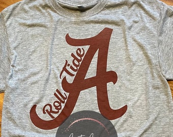 May include: Gray t-shirt with a maroon "Roll Tide" and "A" graphic. The shirt has a small circle logo that says "Aunt Ari's Boutique".
