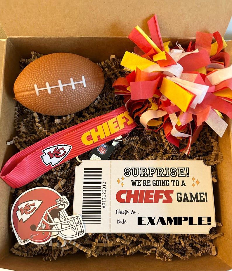 K&ouml;nnte beinhalten: Eine Geschenkbox gef&uuml;llt mit Artikeln zum Thema Kansas City Chiefs, darunter ein roter und gelber Pompon, ein rotes Lanyard mit dem Chiefs-Logo, ein Football, ein Aufkleber eines Chiefs-Helms und ein Ticketstub, auf dem "&Uuml;berraschung! Wir gehen zu einem Chiefs-Spiel!" steht.