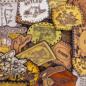 May include: A collection of leather patches featuring various designs, including a truck, a band, a flower, and the words "Doe Out, Bow Out". The patches are all in shades of brown and yellow and have a distressed look.