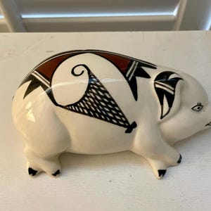 May include: A ceramic pig figurine with a white base, adorned with black, brown, and white geometric patterns. The pig has small black feet and a detailed eye, showcasing a handcrafted aesthetic. This decorative item is suitable for home decor.
