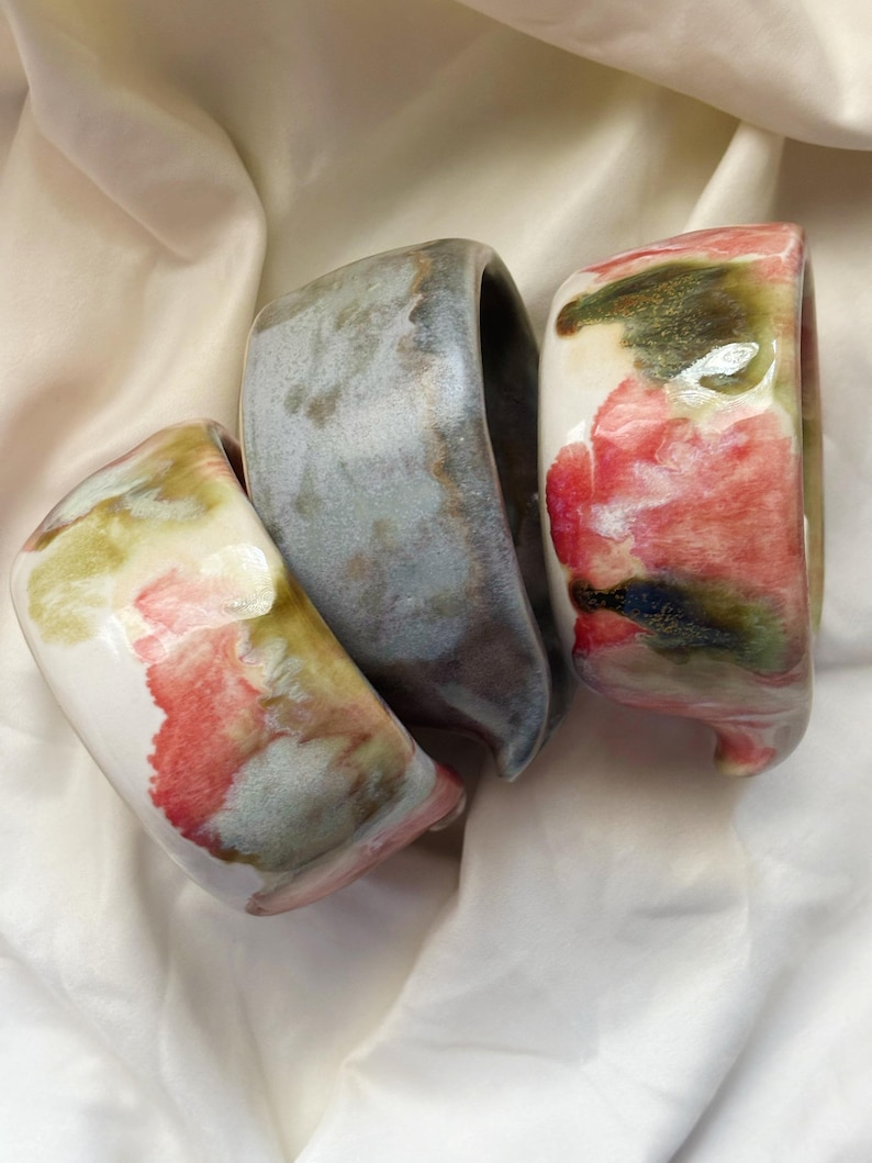 May include: Three ceramic bowls with irregular, organic shapes and glossy finishes. One bowl features a white base with red and green watercolor-style splotches, another is a solid muted grey, and the third has a white base with red and green accents.