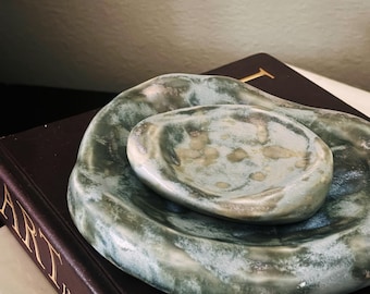 May include: Two nested, hand-formed ceramic dishes with an irregular, organic shape. The glaze features a mottled blend of sage green, deep forest green, and creamy white tones, creating a textured, stone-like appearance with a glossy finish.