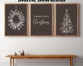 May include: Three framed prints with a Christmas theme. The prints feature a wreath, a Christmas tree, and the text "A Merry Little Christmas" in white on a dark brown background. The frames are a light brown color.