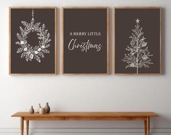 May include: Three framed art prints with a Christmas theme. The prints feature a white wreath, the text "A Merry Little Christmas", and a Christmas tree design, all on a dark brown background. The frames are a light brown color.