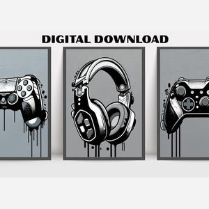 Op de afbeelding: Drie ingelijste digitale kunstprints met gaming-thema illustraties. De prints tonen een gamecontroller, een koptelefoon en nog een controller, allemaal in zwart-wit met een grijze achtergrond en een druipverfeffect. De tekst "DIGITALE DOWNLOAD" staat bovenaan.