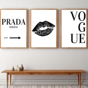 Könnte beinhalten: Drei gerahmte Kunstdrucke mit minimalistischem Design. Die Drucke zeigen die Wörter "PRADA MARFA" mit einem Pfeil, einen schwarzen Lippenabdruck und das Wort "VOGUE" in fetten schwarzen Buchstaben, alles vor weißem Hintergrund.