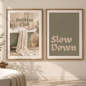 Peut inclure: Deux cadres muraux en bois clair. L'affiche de gauche montre une baignoire vert sauge avec de la mousse, une serviette blanche et le texte Bubbles Club. L'affiche de droite présente un fond vert sauge avec le texte beige Slow Down.