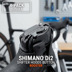 May include: Black Shimano Di2 shifter hoods button booster. The image shows a close-up of a bicycle component with the text "4-PACK BUNDLE" and "SHIMANO Di2 SHIFTER HOODS BUTTON BOOSTER". The component is black and has a textured surface.
