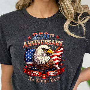 May include: Dark gray t-shirt featuring a patriotic design for the 250th anniversary. The graphic includes an American flag, an eagle, and the text "250th Anniversary", "1776", "2026", and "No Kings Here".