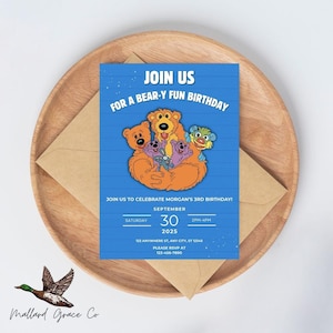 Pode incluir: Um convite de aniversário azul com o texto "JOIN US FOR A BEAR-Y FUN BIRTHDAY" e ursos de desenho animado. O convite inclui detalhes para uma celebração de 3º aniversário, data, hora e informações de RSVP. O convite está em um prato de madeira com um envelope marrom.