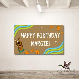 May include: A brown rectangular sign with the text "HAPPY BIRTHDAY MARGIE!" in white. The sign features a cartoon image of Scooby-Doo, orange flowers, and blue and green wavy lines. The sign is for a birthday.