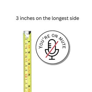May include: A round sticker with the text "YOU'RE ON MUTE" and a microphone icon with a red line through it. The sticker is approximately 3 inches (7.6 cm) in diameter. A yellow measuring tape is next to the sticker.