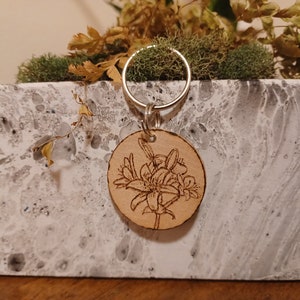 May include: A wooden keychain with a laser-engraved design of a flower bouquet. The keychain is attached to a silver key ring.