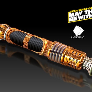 May include: A gold lightsaber hilt with intricate details and a black, ribbed section. The hilt has a textured, metallic finish and a circular, decorative end cap. The text "STAR WARS DAY MAY THE 4TH BE WITH YOU" is visible in the background.