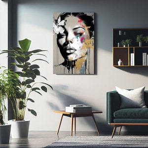 May include: Abstract portrait art print of a woman's face with a butterfly in her hair. The artwork features a grayscale face with colorful paint splatters in pink, blue, and gold. Black paint drips down from the bottom of the canvas.