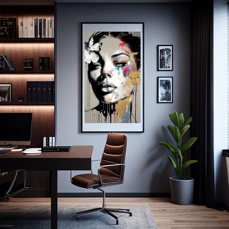 May include: A framed art print featuring a woman's face with a butterfly and colorful paint splatters. The artwork is in a black frame and hangs on a gray wall. The room also includes a desk, chair, and a potted plant.
