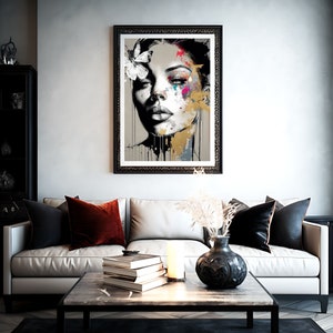 May include: A framed art print featuring a stylized portrait of a woman with a butterfly in her hair. The artwork uses a grayscale palette with splashes of color and gold accents. The print hangs above a white sofa with decorative pillows.