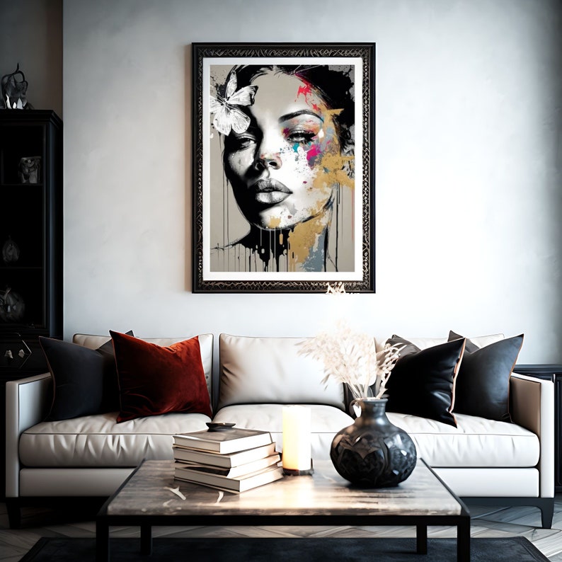 May include: A framed art print featuring a stylized portrait of a woman with a butterfly in her hair. The artwork uses a grayscale palette with splashes of color and gold accents. The print hangs above a white sofa with decorative pillows.