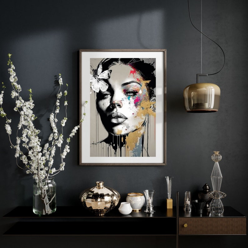 May include: A framed art print featuring a woman's face with abstract paint strokes in gold, pink, and blue. A white butterfly adorns her hair. The artwork hangs above a black console table with decorative vases and a hanging light fixture.