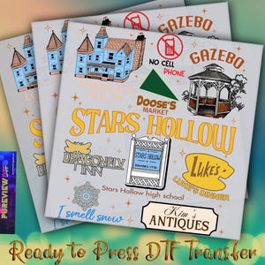 May include: A stack of ready-to-press DTF transfers featuring a design with the text "Stars Hollow" and various illustrations, including a gazebo, Dragonfly Inn, and Luke's Diner. The design includes the text "I smell snow" and "Kim's Antiques".