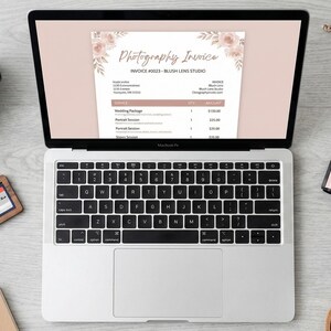 May include: A laptop displays a photography invoice with floral accents. A camera, lens, memory card, film rolls, and a cup of coffee are arranged around the laptop. Dried flowers add a decorative touch to the scene, suggesting a photography studio.