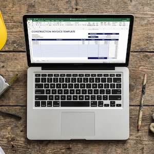 Può includere: Un laptop che mostra un modello di fattura di costruzione è su una superficie di legno, circondato da un casco giallo, planimetrie arrotolate, un metro a nastro, guanti da lavoro e una matita. La scena suggerisce lavori di costruzione o architettura.