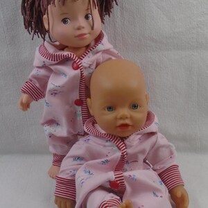 Puede incluir: Dos mu&ntilde;ecas beb&eacute;s con pijamas rosas a juego con estampado floral y ribetes a rayas rojas y blancas. Una mu&ntilde;eca tiene cabello casta&ntilde;o y la otra es calva. Las mu&ntilde;ecas est&aacute;n posadas sobre un fondo blanco.