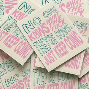Puede incluir: Un montón de tarjetas de color crema con el texto "NO ONE KNOWS WHAT THE FUCK THEY'RE DOING JUST KEEP GOING" en verde azulado y rosa. Las tarjetas están dispersas, algunas se superponen, mostrando el diseño.