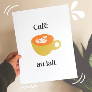 May include: A white print featuring a yellow coffee cup with orange coffee and white foam art. The words "Café au lait" are printed in black, with decorative white lines and splashes.
