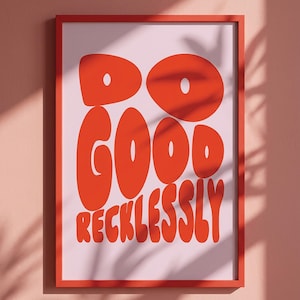 Op de afbeelding: Een rechthoekige wandkunstprint in een rode lijst met de tekst DO GOOD RECKLESSLY in dikke, afgeronde, oranje-rode letters tegen een lichtroze achtergrond. Het ontwerp maakt gebruik van een speels lettertype in bubbelstijl.
