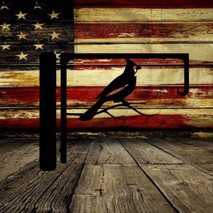 May include: Black metal decorative bird feeder bracket with a cardinal silhouette. The bracket is mounted on a wooden surface in front of a distressed American flag background. The design is suitable for outdoor use.