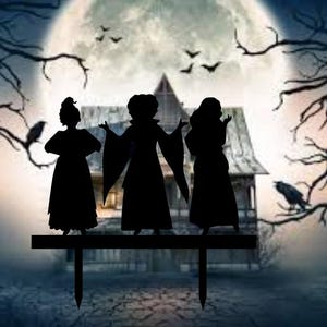 May include: Three black silhouette figures of women dressed in long gowns, standing on a black platform in front of a dark, foggy background with a full moon and trees.