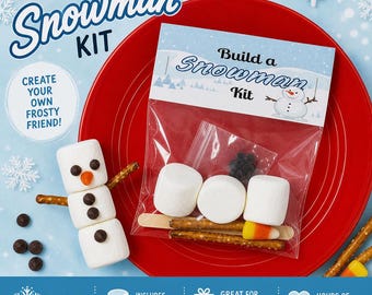 May include: A Build a Snowman Kit in a clear plastic bag containing white marshmallows, pretzel sticks, candy corn, and dark chocolate chips. A finished marshmallow snowman with pretzel arms and chocolate chip features sits beside the kit.