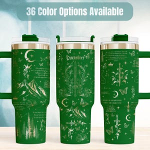 May include: Three green tumblers with handles and clear lids, featuring gold-toned line art of swords, mountains, butterflies, moons, and books. The text 36 Color Options Available appears at the top, with Quicksilver printed on the center tumbler.