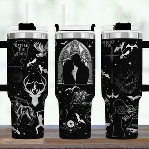 May include: Black travel tumbler with a silver lid and handle, featuring white illustrations of silhouettes, animals, and text. The tumbler has a straw and a black handle. The text includes "Rattle the Stars" and "You Do Not Yield."