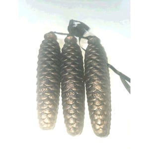 May include: Three elongated, metallic, bronze-toned pinecone-shaped weights with a textured, scale-like surface. Each piece features the embossed number 1170 near the base and is attached to a black cord for hanging, creating a uniform set.