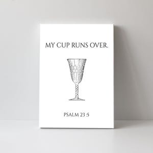 Puede incluir: Una impresión en lienzo blanco con el texto "MY CUP RUNS OVER." y "PSALM 23:5" en negro. Una ilustración detallada de una copa de vino está centrada en el lienzo. La copa tiene un patrón decorativo y un tallo retorcido.