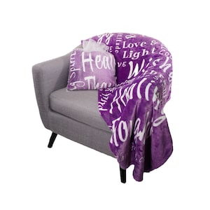 May include: Purple plush throw blanket with white text that reads "Love & Light, Gratitude, Wish, Heal, Thank, Hope, Joy, Peace, Spirit". The blanket is draped over a gray armchair with a matching purple pillow.