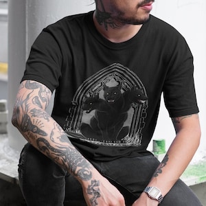 May include: A black t-shirt with a graphic of a black, four-legged creature with horns emerging from a stone archway.