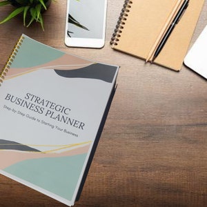 May include: A closed spiral bound book with a colorful abstract design on the cover. The title of the book is "Strategic Business Planner" with the subtitle "Step-by-Step Guide to Starting Your Business".