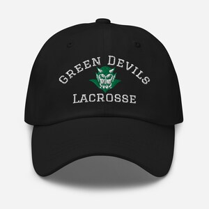 May include: Black baseball cap with the text "GREEN DEVILS LACROSSE" in white, arched across the top. A green devil head logo is centered above the word "LACROSSE". The cap has a curved brim and a button on top.