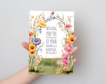 May include: A rectangular greeting card featuring a watercolor illustration of a wildflower archway. The text reads: WISHING YOU THE Wedding Day OF YOUR DREAMS & A BEAUTIFUL life together! The flowers are yellow, purple, pink, and orange.